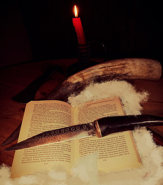 Buch mit Schwert vor Kerze und Horn